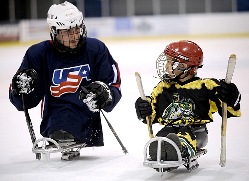 Two disabled children in full hockey gear out on the ice rink in their skate chairs
