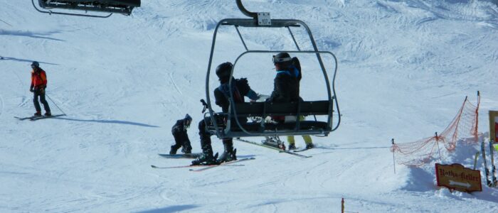 A disabled skier in a ski chair and companion ride a chairlift near the base of Taos Ski Valley.