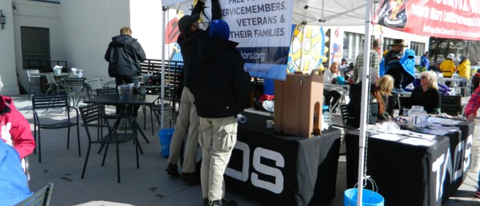 Staff fixes yoga banner on white Not Forgotten Outreach tent at the base of Taos Ski Valley in front of lodge.